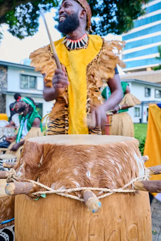 A drummer in a raffia costume plays a hide drum