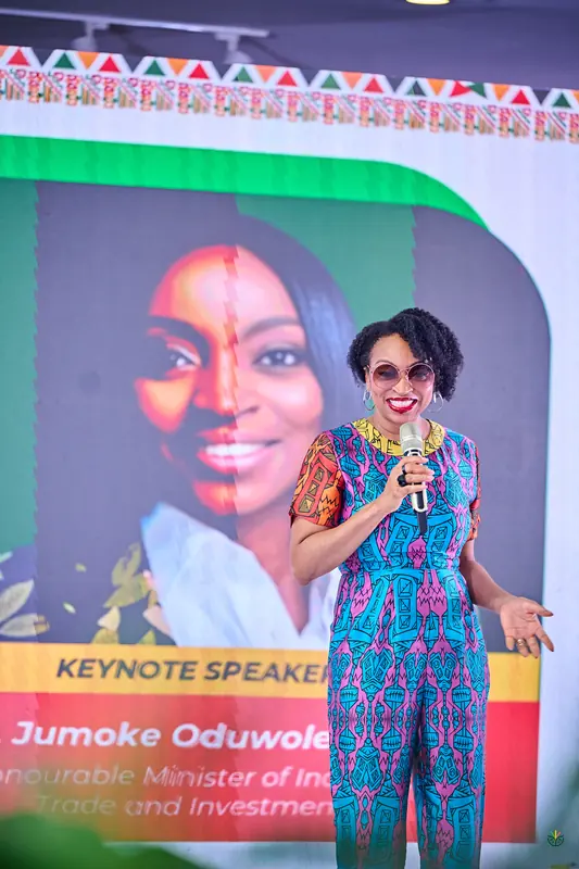 Keynote speaker on stage in a patterned jumpsuit, her portrait on the screen behind