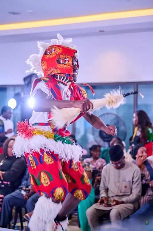 A masquerade dancer in red and white performs beside the audience